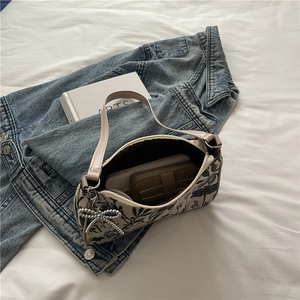 Floral canvas underarm bag with pearl bow charm and leather handle on denim background
