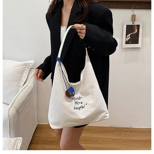 Detail of white canvas tote bag with black lettering and blue mini bucket charm