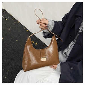 Detailed shot of glossy brown leather shoulder bag with a gold metal buckle on a model