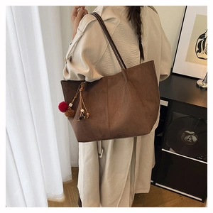 Detail of a large brown suede tote bag with a decorative tassel charm on a model's shoulder