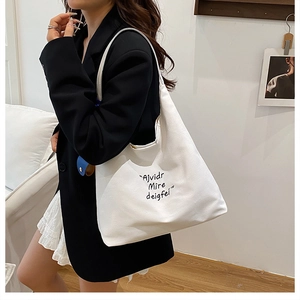 Detailed view of large white canvas tote bag with black embroidery on a model