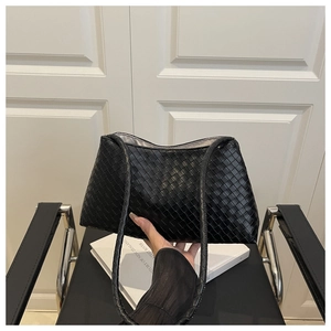 Close-up of black woven shoulder bag with intricate texture in a minimalist setting