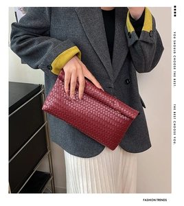 Détail d'une pochette tissée rouge portée avec un blazer gris et une jupe plissée
