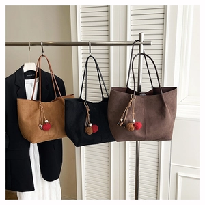 Close-up of suede tote bags in camel, black, and brown with decorative pom-pom charms