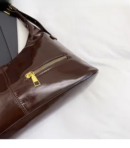 Detail einer dunkelbraunen Lackleder-Handtasche mit glänzender Textur und Goldreißverschluss