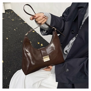 Detail of a dark brown glossy leather hobo bag with a gold rectangular metal buckle