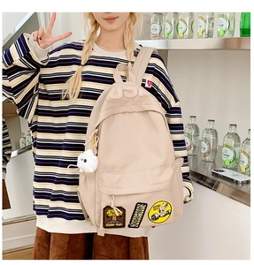 Detailed view of beige backpack with patches and white plush pendant on a female model