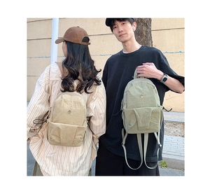 Macro detail of beige and green nylon backpacks with metal logo and side drawstring