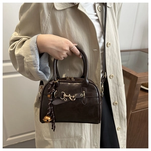 Close-up of vintage brown crossbody bag with gold horse-bit and bell charm detail