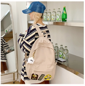 Close-up of beige backpack featuring USA embroidery and plush sheep charm on side pocket