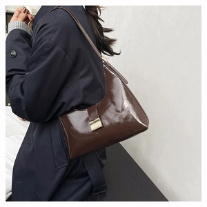 Detail of dark brown glossy leather underarm bag with minimalist gold metal buckle