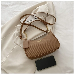 Détail d'un sac sous le bras tissé marron avec chaîne dorée sur blazer beige