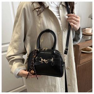 Detail of black leather shell bag with gold hardware and woven charm on beige trench coat