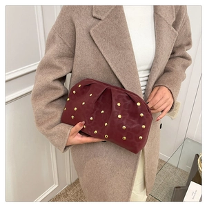 Detail of burgundy ruched dumpling clutch bag with gold studs held by a model