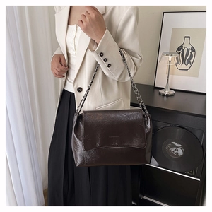 Détail d'un sac bandoulière chic en cuir noir texturé avec chaîne argentée sur un modèle