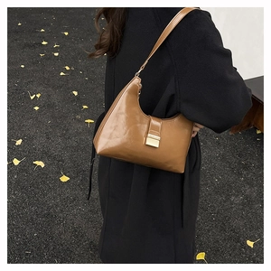 Close-up of brown leather shoulder bag with metallic buckle in an autumn street setting
