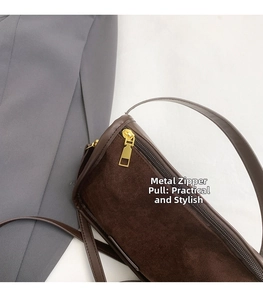 Detail of golden metal zipper pull on brown matte leather handbag with grey fabric background