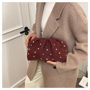 Detail of burgundy leopard embossed handbag with gold rivets held by a woman in beige coat
