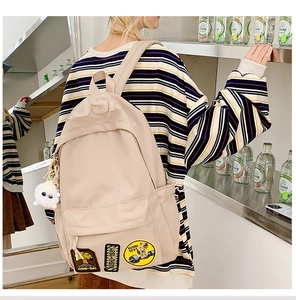 Detail of beige nylon school backpack with retro patch and cute plush lamb keychain