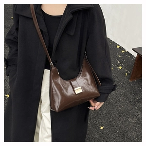 Detail of dark brown glossy leather hobo bag with a golden metal buckle on leaf ground