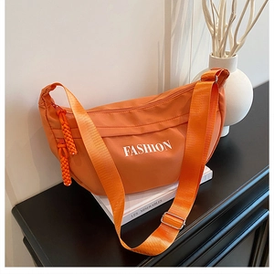 Detail of vibrant orange nylon crescent bag featuring white FASHION print and woven zipper pull