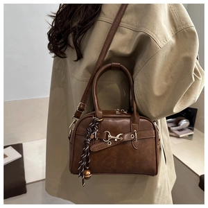 Detail of vintage brown leather bag with golden bell charm and adjustable shoulder strap