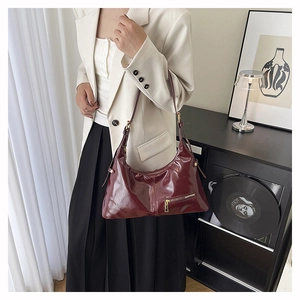 Close-up of a burgundy glossy shoulder bag with golden zipper details and adjustable strap