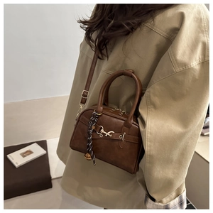 Brown vintage faux leather handbag with metal buckle and braided strap worn by model