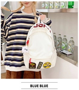 Detail of white canvas backpack with embroidery patches, red USH logo and plush charm