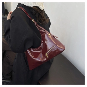 Detail of burgundy vintage hobo bag with glossy finish and gold zipper on a model