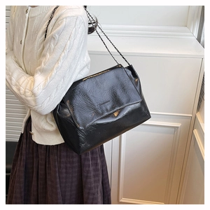 Détail du sac bandoulière en cuir verni plissé noir avec chaîne en métal sur modèle