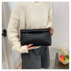 Vue détaillée de la pochette en cuir tressé noir tenue par un mannequin en intérieur