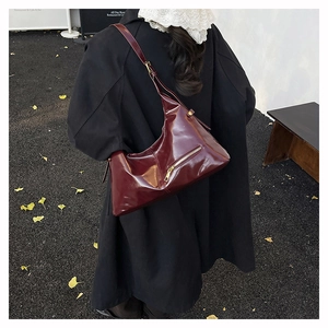 Detail view of burgundy glossy leather shoulder bag with chic asymmetrical design and zipper