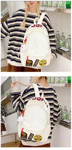 Detail of white canvas backpack with USHU embroidery patches and plush doll pendant