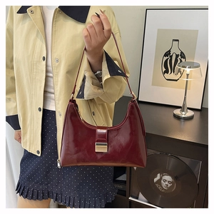 Detail of burgundy leather shoulder bag with gold metal buckle in retro indoor setting