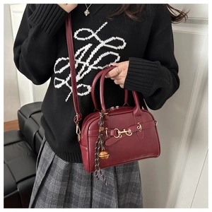 Detail of burgundy leather shoulder bag with golden horsebit buckle and bell pendant