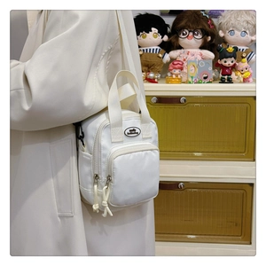 Close-up of a white mini nylon crossbody bag with black logo and rope zipper pulls