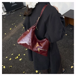 Close-up of a burgundy glossy leather shoulder bag with gold zipper detail on model