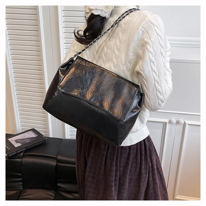 Détail d'un sac à bandoulière en cuir noir brillant avec chaîne et rabat au style rétro