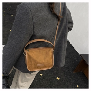 Detail view of brown faux suede crossbody bag styled with a grey coat and autumn leaves