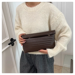 Détail de la texture en cuir tressé marron foncé sur une pochette avec ferrures dorées