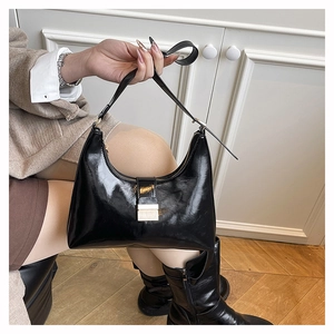 Close-up of black glossy patent leather shoulder bag with golden metallic buckle