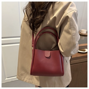 Model wearing a burgundy leather crossbody bag with a modern rectangular design