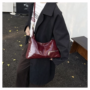 Detail of burgundy glossy leather shoulder bag with gold zipper on a black coat outfit