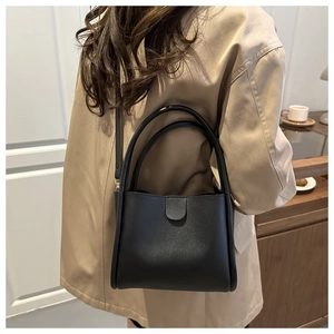 Minimalist black leather bucket bag worn by model over a classic beige trench coat