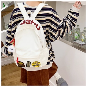 Detailed close-up of white canvas backpack with red lettering and vintage embroidery patches