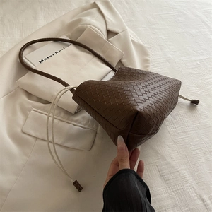 Deep brown hand-woven leather shoulder bag with drawstring closure on white blazer