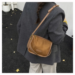 Close-up of brown suede saddle bag with decorative leather patch and metal hardware detail