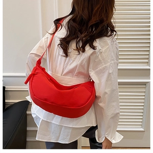 Detail of red crescent-shaped crossbody bag with adjustable wide strap on model