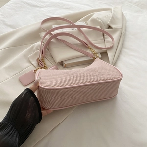 Pink woven baguette shoulder bag with gold chain strap on white blazer background